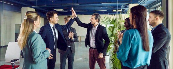 Group of positive business people, colleagues and coworkers, giving high five and celebrating...
