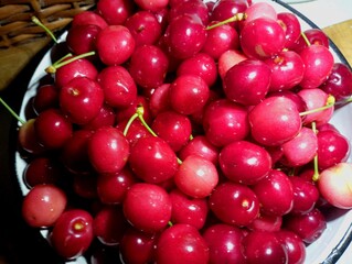 A large round bowl is filled with juicy ripe red cherries. Beautiful cherry berries are fresh and tasty with many vitamins. Theme of seasonal berries and fruits.