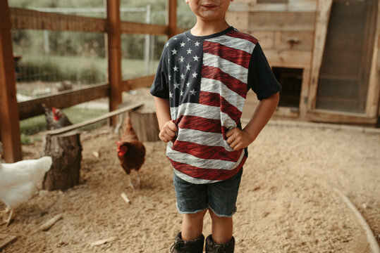 Child in American flag shirt standing in a chicken coop with chickens