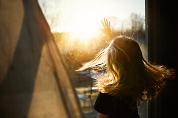 Young girl reaching for sunbeams in bright window