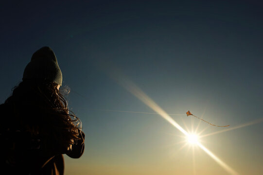 Back view of young girl flying kite against sunny sky