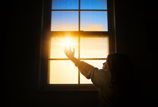 Young girl reaching toward sunlight shining through window - Powered by Adobe