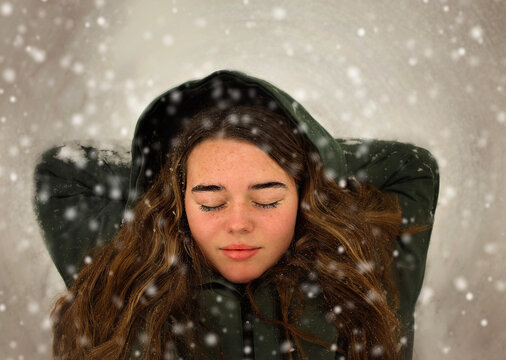 Beautiful teen girl laying with closed eyes in falling snow