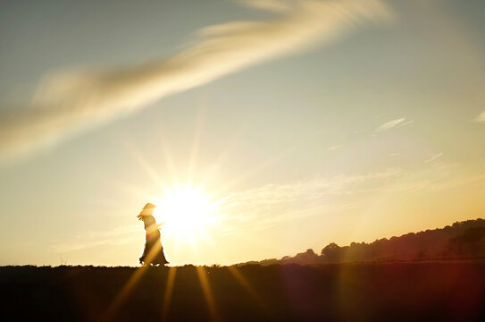 Young girl walking into bright sunset on hill