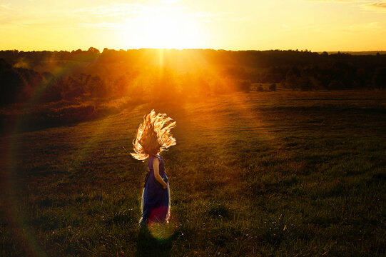Young girl flipping hair in field at sunset