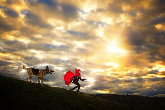 Young girl in red cape running from German Shepherd