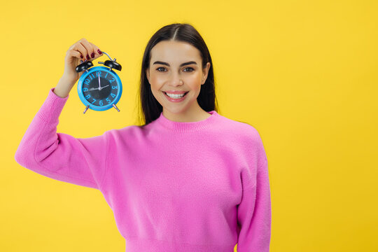 Daylight saving time. Beautiful woman showing an alarm clock and looking happy about the time change