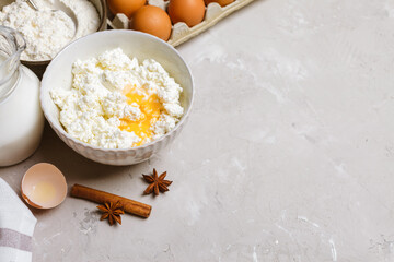 Cottage cheese in a ceramic bowl, jug of milk, flour, eggs and spices. Ingredients for cooking. Copy space for text