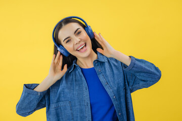 Cheerful lady in casual denim shirt dancing and singing carelessly over yellow studio background....