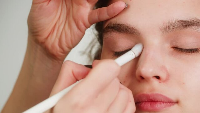 Eye shadow makeup to the upper eyelid, close-up. Makeup artist applies a bright eye shadow with a make-up brush.Tutorial master class of professional makeup, smoky eyes 