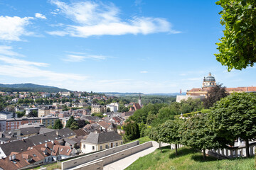 Naklejka premium Scenic view of Melk town with Melk Abbey in the background under a bright blue sky, surrounded by lush greenery and historical buildings
