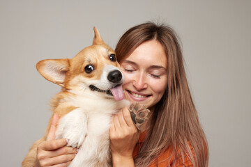 a brunette girl holds and hugs a red corgi dog on a clean light background, the concept of love for...