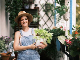 A smiling woman in a hat happily embraces home gardening, holding a potted plant