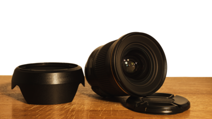 Wide-angle lens of a 24 mm SLR camera with a bend and a cap next to it on a plank surface isolated.