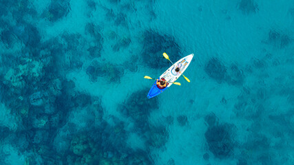Aerial view of a woman and a young man kayaking on clear blue waters at Andaman Island. She does...