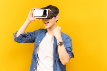 Asian young man in jacket jean and playing video games using vr with headphones on yellow background isolated.