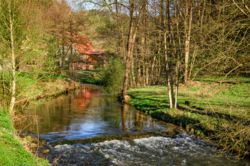 Romantischer Flusslauf mit kleiner Staustufe und rotem Haus in der Fränkischen Schweiz, Deutschland