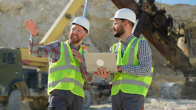 Two men workers in uniform with laptop are talking at the stone quarry
