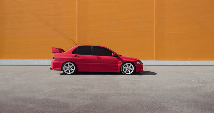 red Mitsubishi Lancer Evolution IX in front of orange wall on a sunny day - side view. Odesa, Ukraine - May 07 2016.
