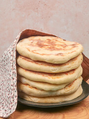 Homemade flatbreads, placed on a brown ceramic plate, on a wooden chopping board, with a sandy background