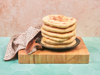 Homemade flatbreads, placed on a brown ceramic plate, on a wooden chopping board set on a green ceramic countertop, with a sandy background - Powered by Adobe