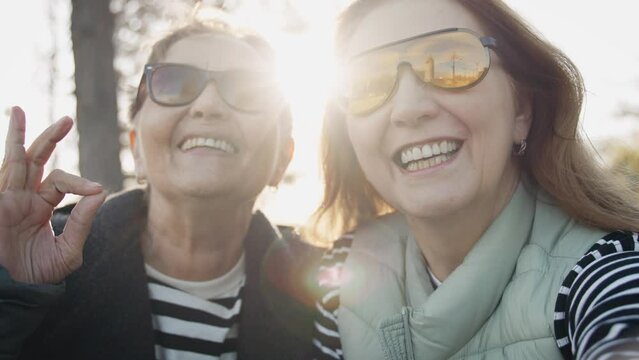 Two adult women friends take selfies together while sitting on a bench in the park