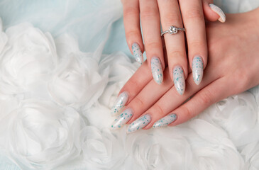 Elegant Hands Featuring Sparkling Ring and Blue Floral Manicure on Delicate White Fabric