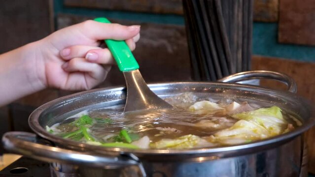 cook fa pho soup vietnam close-up deep frying pan in which broth is cooked pork bones rice vermicelli and greens girl stirs her food in a restaurant buffet selection of ingredients in cooking Vietnam