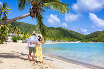 Happy holiday couple with sunhats enjoys a tropical beach with palm trees surrounded by rain forest in the Caribbean, Antigua island