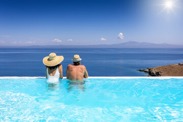 A couple swimming in an infinity pool and enjoying the view to the blue, mediterranean sea during summer vacation time