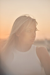 A blonde woman is facing a sunset, with her face obscured and a soft, warm glow