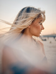 A blonde woman's hair is swept by the wind at dusk, with her face blurred out for privacy