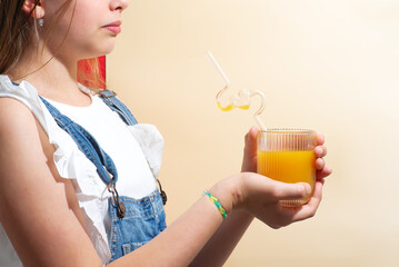 A girl is sitting at a table holding a glass of orange juice with a straw