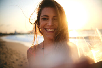 Sunlit portrait of a young woman smiling at the camera with the beach as a backdrop during sunset