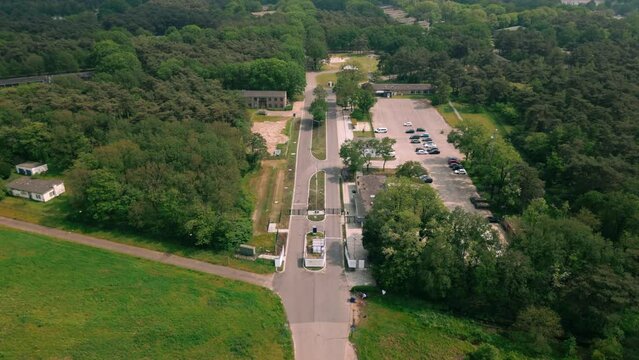 Aerial footage of the entrance to Budel asylum refugee camp, showing the gate, surrounding fences, and nearby buildings. Captured from above, highlighting the camp's layout and security.