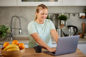 Young woman wearing casual clothes using laptop and drinking coffee in the kitchen