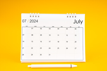 July 2024, Monthly desk calendar for 2024 year and pen on yellow background.