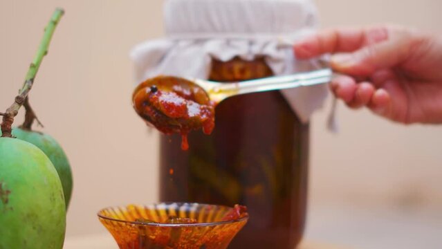 Close up shot of Indian woman hand taking Mango Pickle with spoon. Indian handmade organic sweet pickle. Aam Achar delicious homemade food.