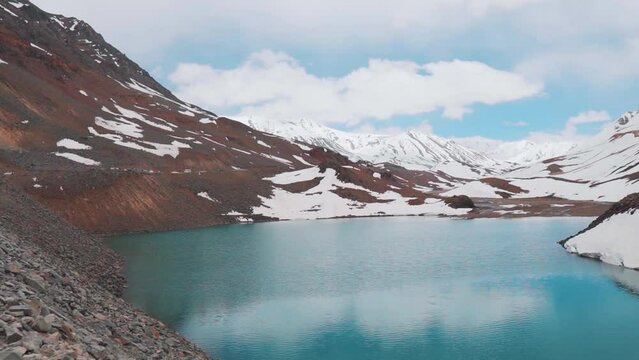Suraj Tal lake with turquoise water and snow covered mountains in Lahaul, Himachal Pradesh, India. Blue calm lake surrounded by snow capped mountains in Indian Himalayas. Reflection of sky in lake