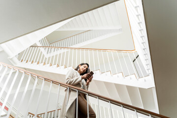 Young woman with smartphone walking down stairs in staircase