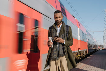 Portrait of stylish man using smartphone next to a train