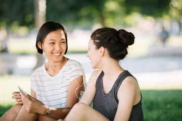 Two friends sitting in city park listening music together with earphones
