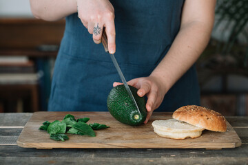 Woman preparing vegan burger, slicing avocado