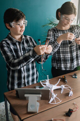 Siblings preparing drone on table while standing at home