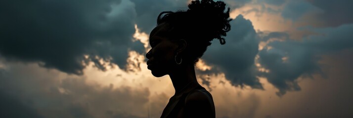 A silhouette of a black woman stands out against a backdrop of dramatic storm clouds as the sun sets, creating a striking contrast - Powered by Adobe