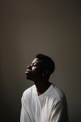 Obraz premium Young African American man in a white shirt, eyes closed, embracing serenity in a dark, minimalist setting, highlighting a calm and contemplative mood.