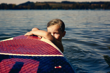Boy with SUP board on a lake at evening twilight
