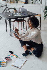 Disigner sitting on ground of her home office, using digital tablet