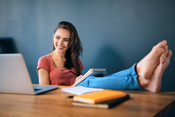 Smiling female entrepreneur with feet up on desk working in home office