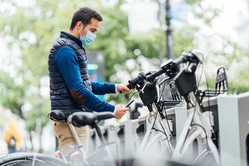 Young man using smart phone at bicycle parking station during coronavirus